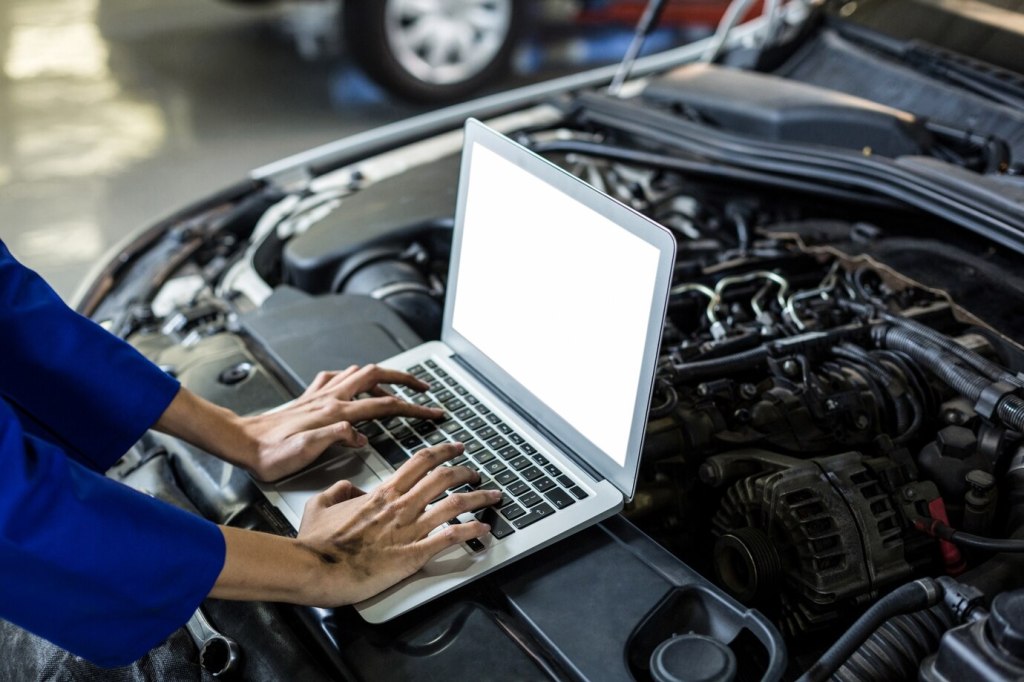 an automotive electrical mechanic running a diagnostic on a car with the hood open
